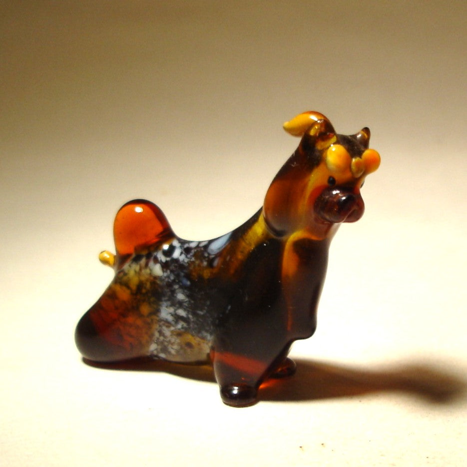 The glass Yorkshire Terrier figurine is displayed from the side, showcasing its flowing coat, poised body and a yellow bow on its head.