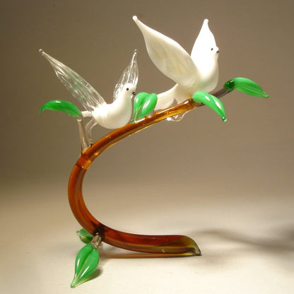 A front view of a glass figurine featuring two white doves perched on a  glass branch, showcasing their outstretched wings in an elegant, peaceful pose.