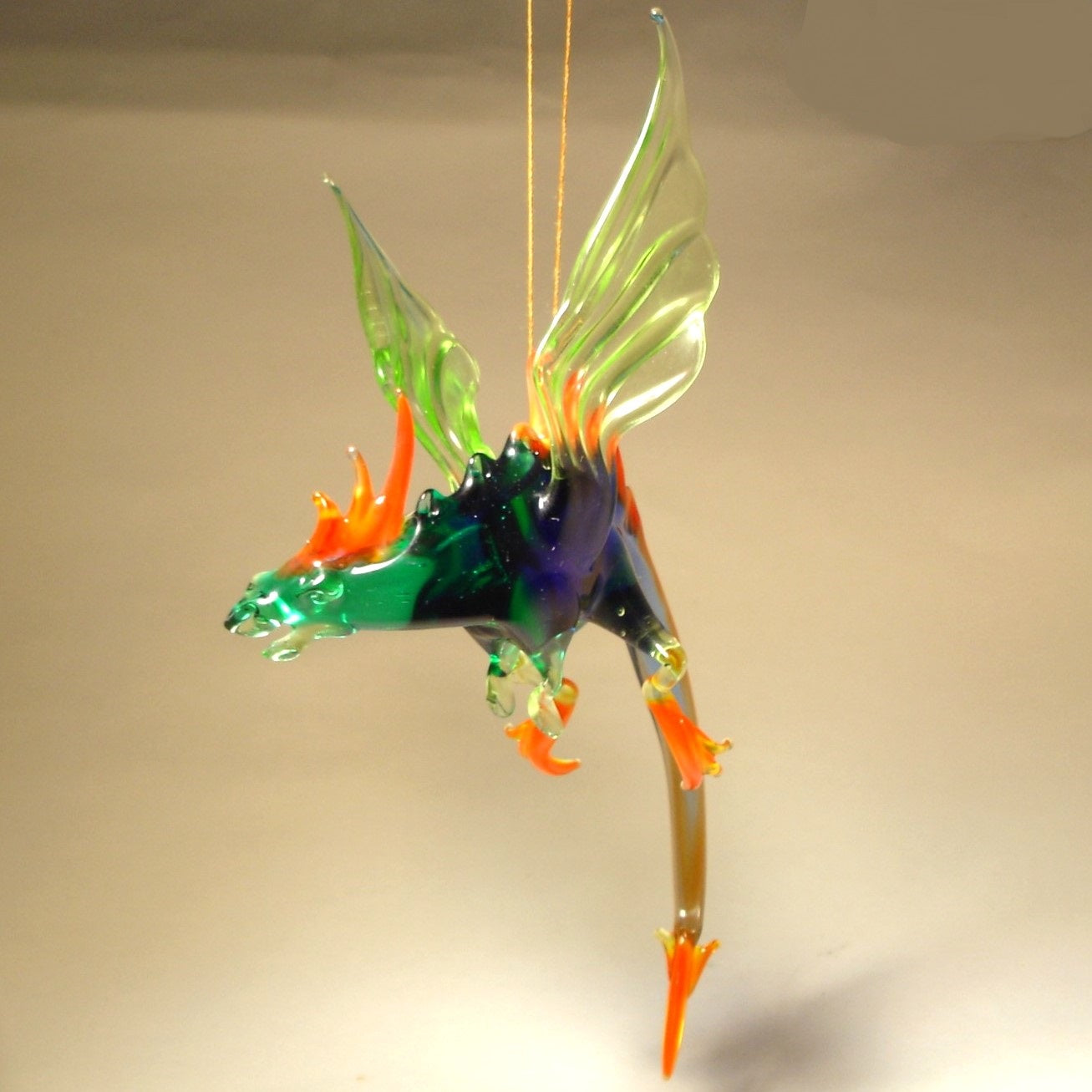 A front view of a glass dragon figurine suspended on a string with intricate wings extending from its back.