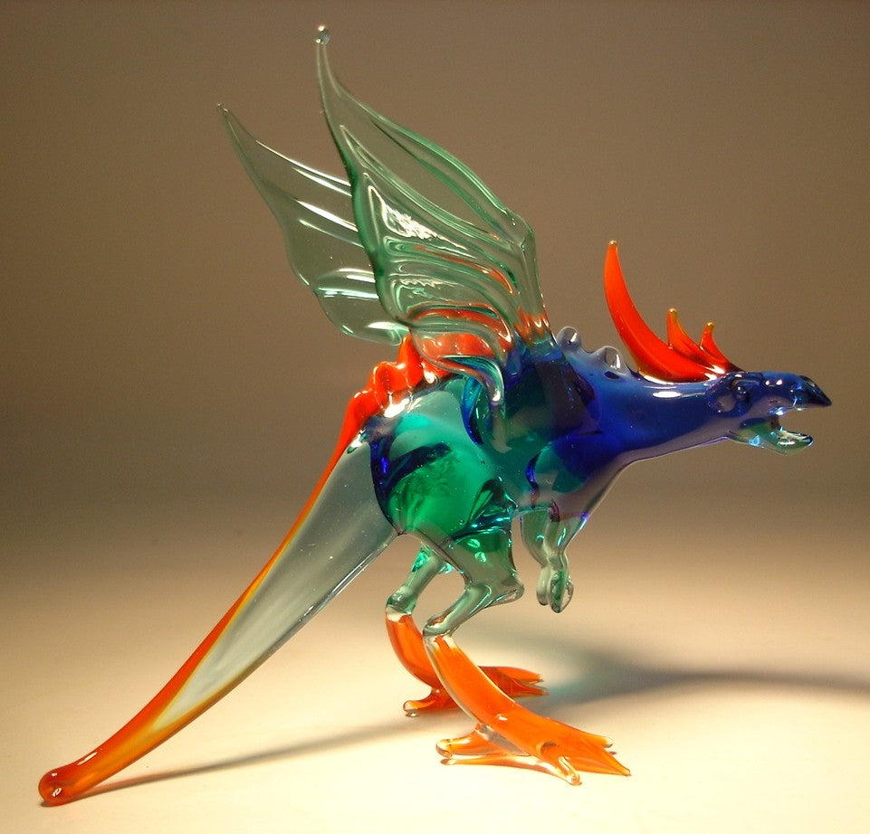 A front view of a glass winged dragon figurine, showcasing its transparent green wings, fierce expression, and detailed body in green and blue. The red ridge runs along the spine. 