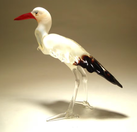 A side view of a glass stork egret figurine, highlighting the smooth lines of its back tipped in black and the delicate curvature of its neck.