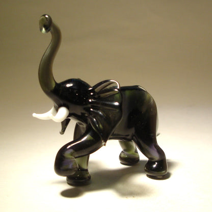 A detailed glass elephant figurine with its trunk raised high and a raised left foot.