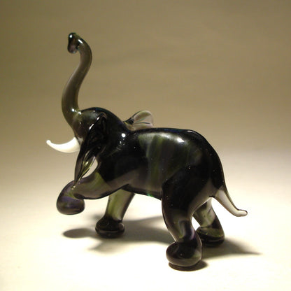 A handcrafted glass elephant figurine standing tall with its trunk elegantly raised, displaying a proud and majestic body posture. 