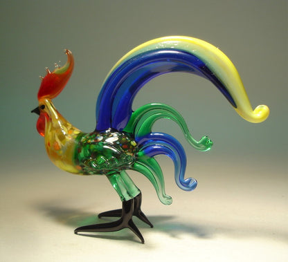 Side view of a glass blue fighter rooster figurine, showcasing its bold stance and vibrant green body with intricate blue and yellow tail.