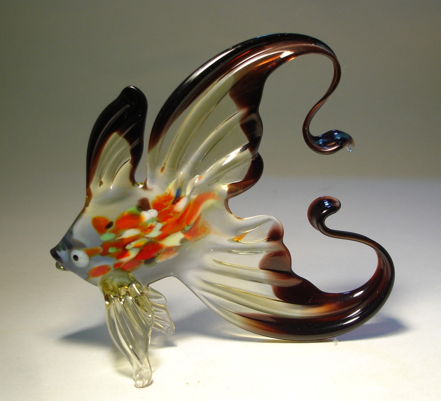 handmade glass fish figurine, highlighting the detailed pattern of colors and the sleek curve of the tail - left side view