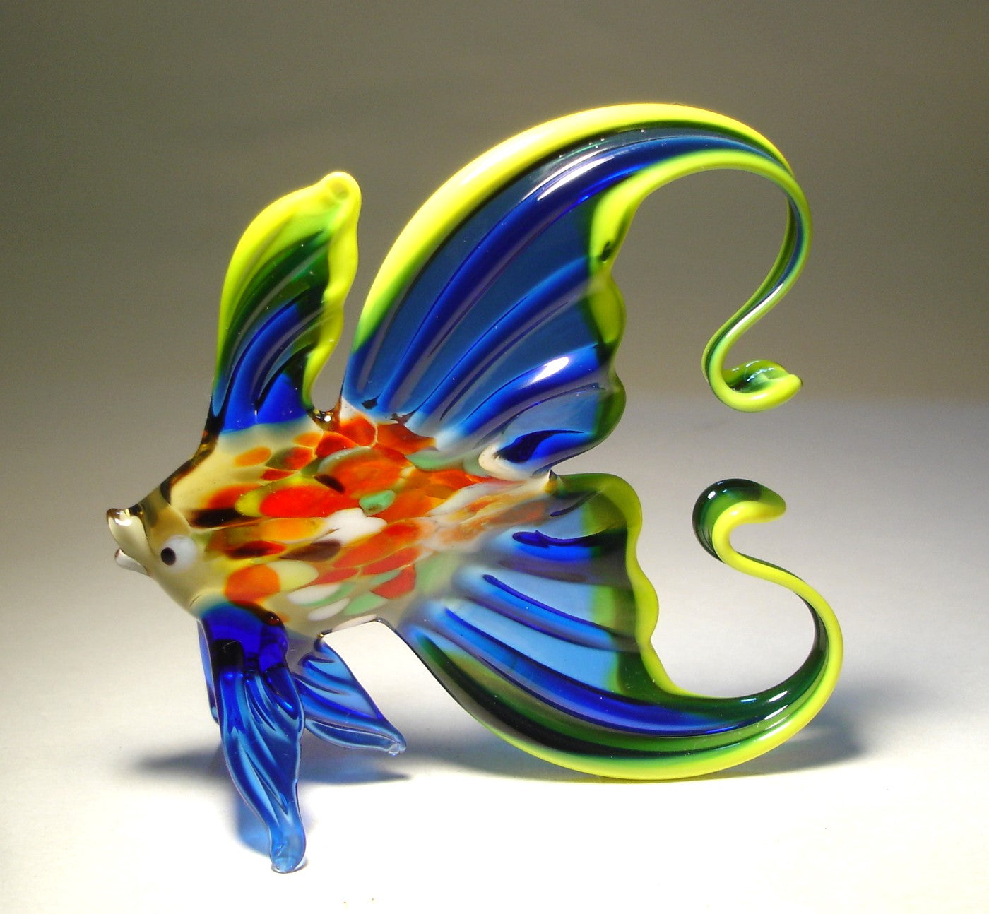 Left side view of the blue glass fish figurine, highlighting the arched tail and the intricate yellow trim along its fins