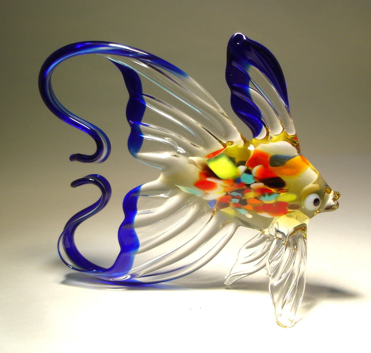 A handmade blue and clear exotic glass fish figurine with an arched tail, showcasing its vibrant colors and elegant form