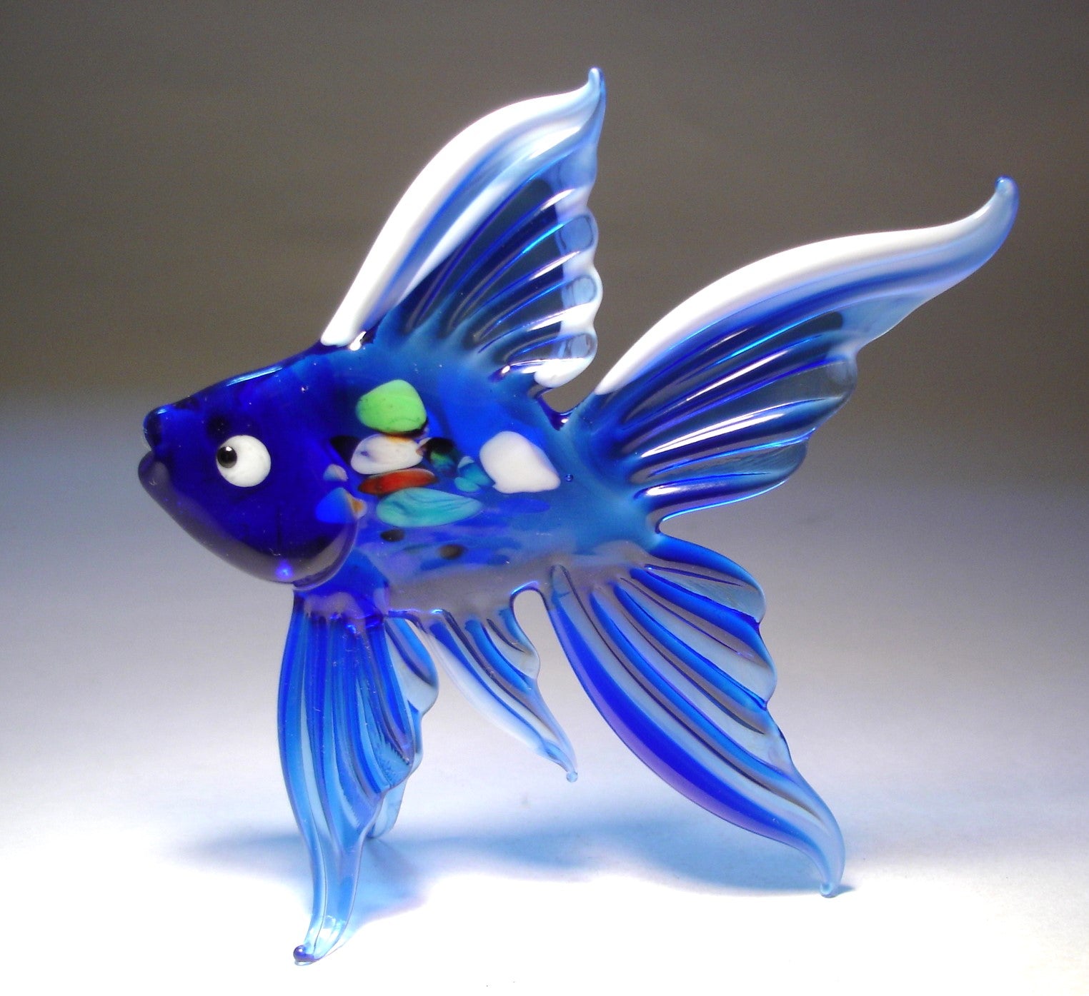 Side view of the blue and white fish figurine, highlighting the elegant curves and multicolored specs on its body