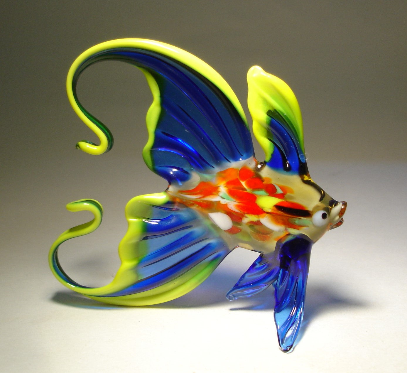 a handmade blue glass fish figurine with an arched tail, trimmed in yellow - right side view