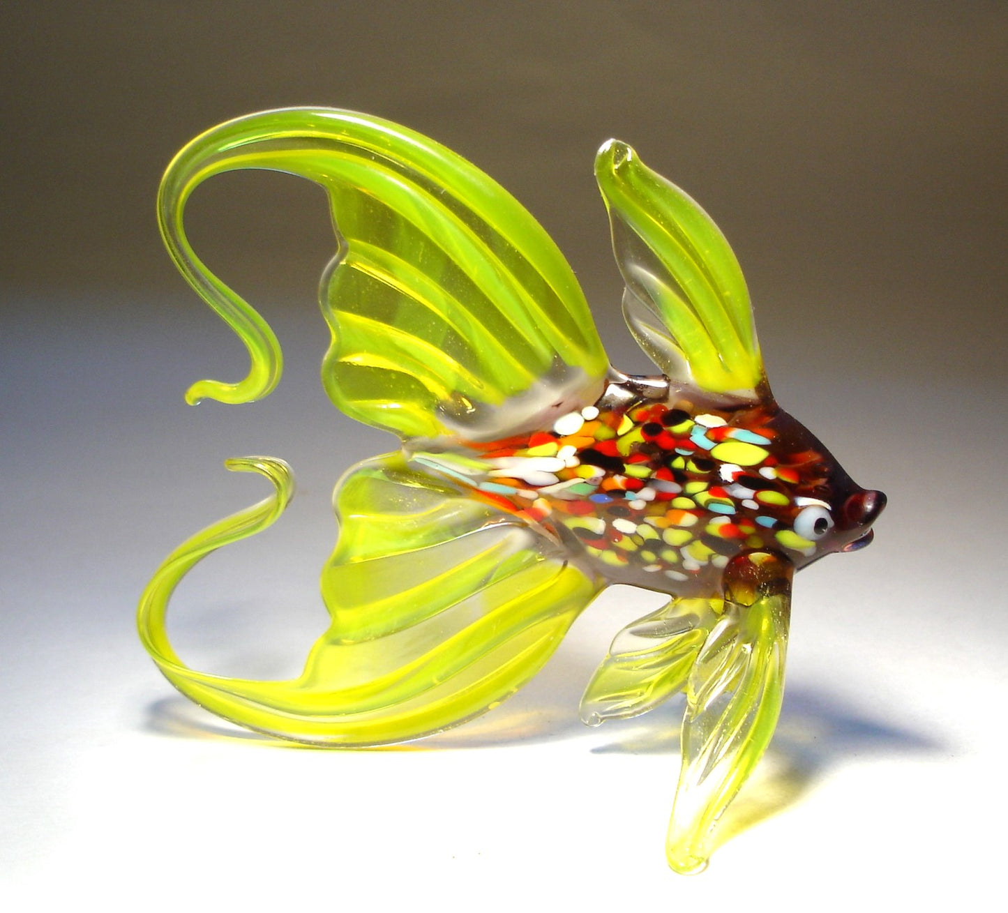 Close-up of a yellow glass fish figurine, featuring a vibrant, multicolored body and an elegantly arched tail. 