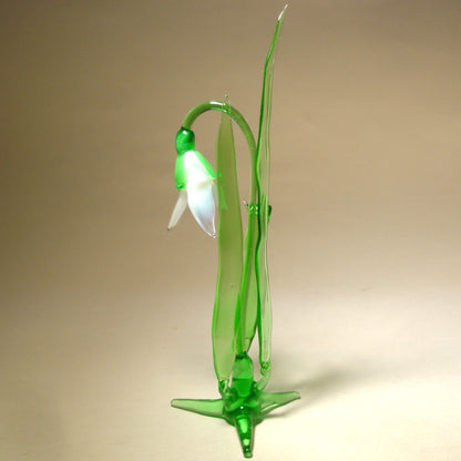 A side view of a glass snowdrop figurine, emphasizing the elegant curves of the petals and the smooth texture of the green stem.