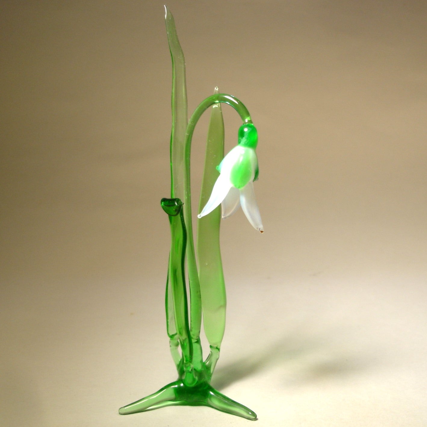 A front view of a delicate glass snowdrop figurine, showcasing its white petals and slender green stem.