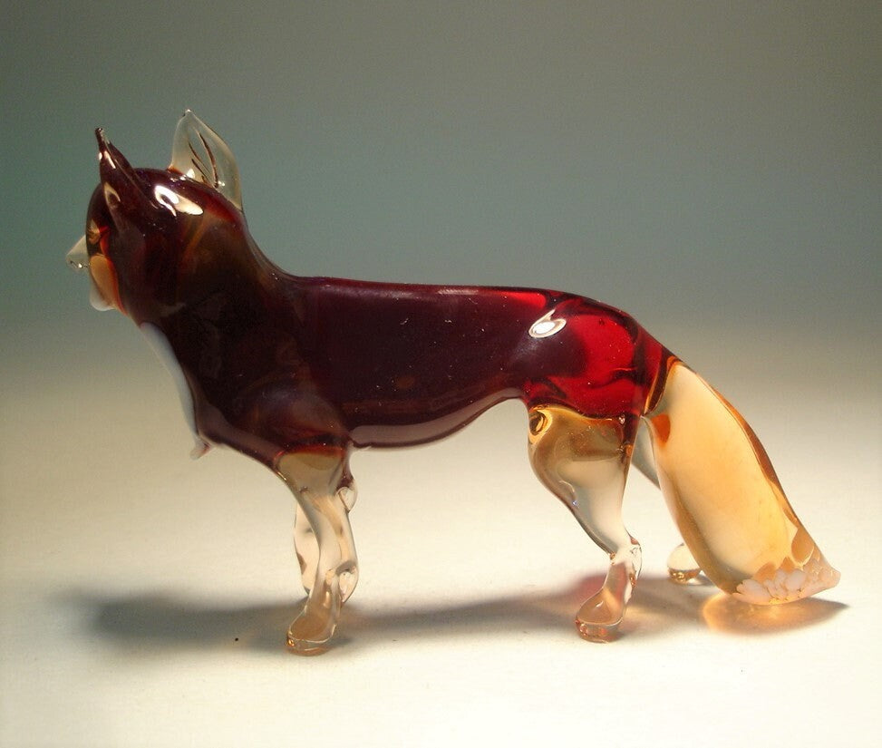 The glass dark red fox figurine sitting gracefully, showcasing its sleek body and bushy tail .