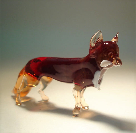 A side profile of a glass dark red fox figurine, displaying its elegant posture. The tail, ears and les are in transparent beige glass.