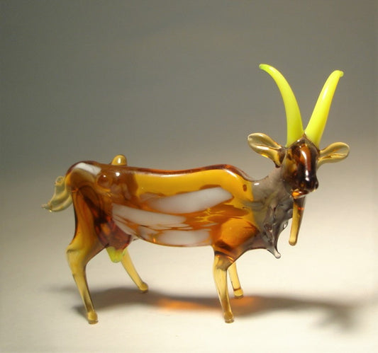 A side view of a brown glass goat figurine, highlighting its slightly curved yellow horns.