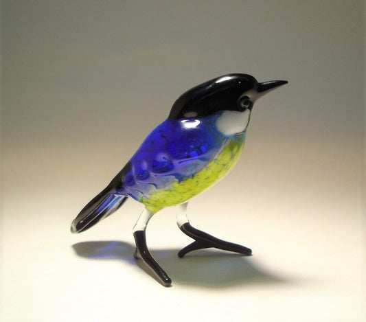 A side view of a glass Great Tit figurine, highlighting its detailed features, including its black beak and bright blue wings.