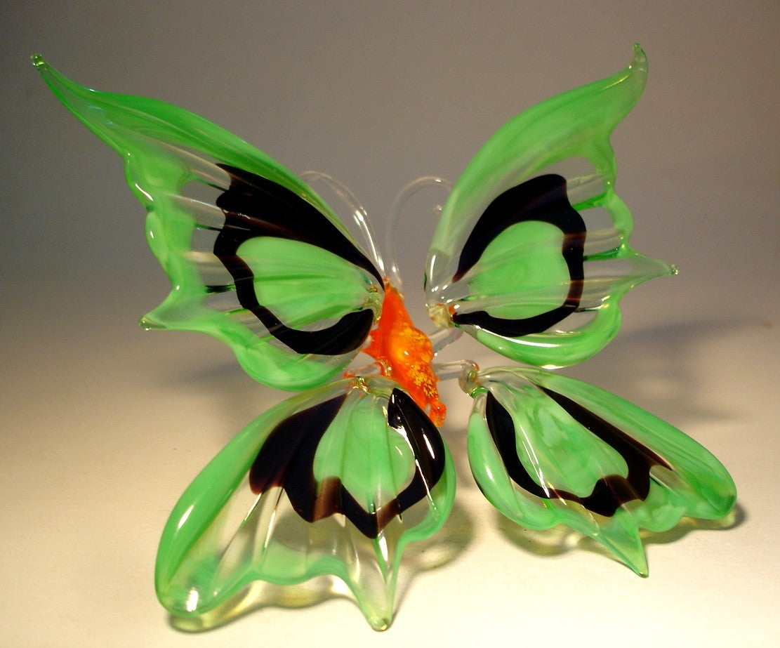 A side view of the glass butterfly figurine, showcasing the slightly raised green and black wings and the butterfly's red body.