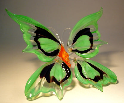 A side view of the glass butterfly figurine, showcasing the slightly raised green and black wings and the butterfly's red body.