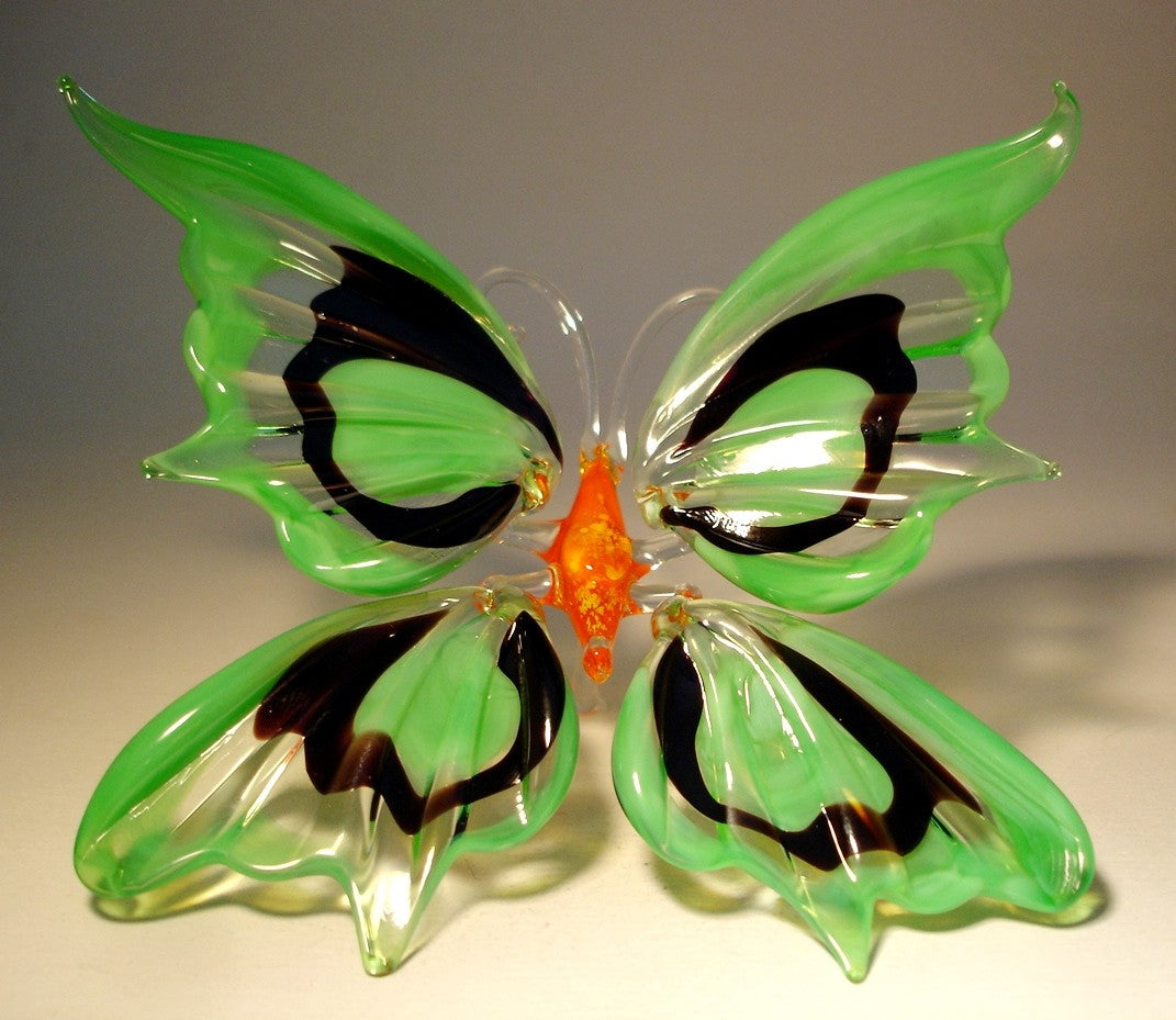 A glass figurine of a butterfly with vibrant green and black wings, sitting gracefully on a surface. 