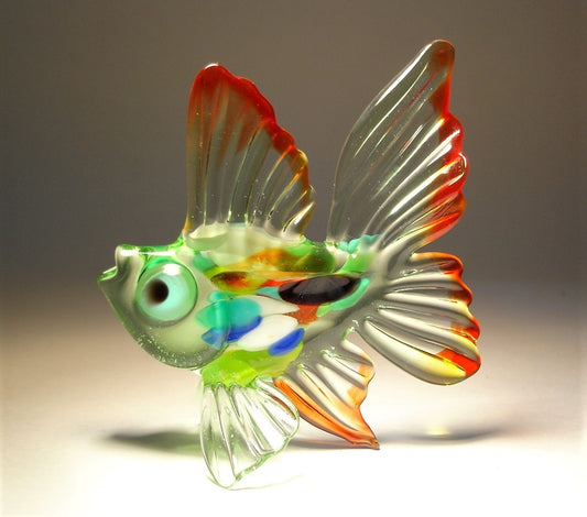 A glass figurine of an exotic fish with a striking green with multicolored body. The fish features wide, flowing fins in light green trimmed with red.