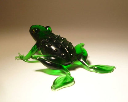 A side view of the green glass frog figurine, highlighting the round body and extended legs positioned as if ready to leap. 