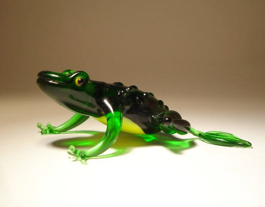 A glass figurine of a frog in vibrant green, sitting upright with wide, glossy eyes and contrasting yellow belly.