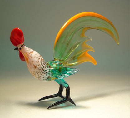 A close-up shot of the green glass rooster figurine, focusing on the intricate detailing of its yellow-trimmed tail and the textured surface of its feathers. 