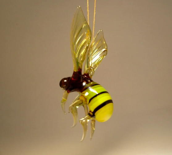 Front view of a glass hanging bee figurine ornament, displaying its yellow and black striped body and clear yellowish wings.