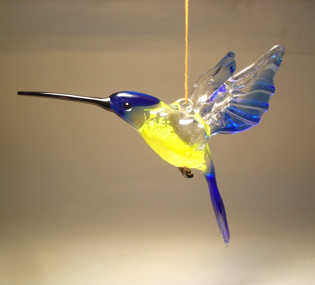 Side view of the blue and yellow glass hummingbird ornament, highlighting elegant shape of its long beak  and blue wings