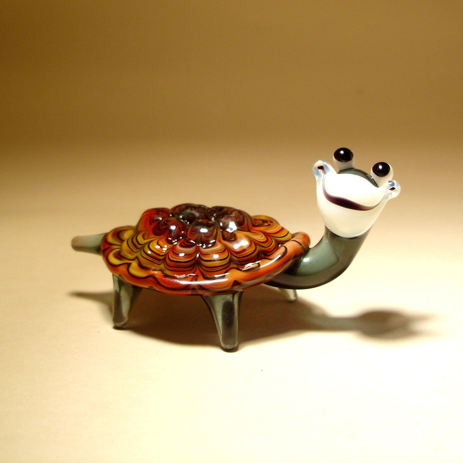 A close-up of the Glass Happy Turtle Tortoise Figurine, showcasing its smiling face and beautifully detailed brown and yellow shell with intricate details.