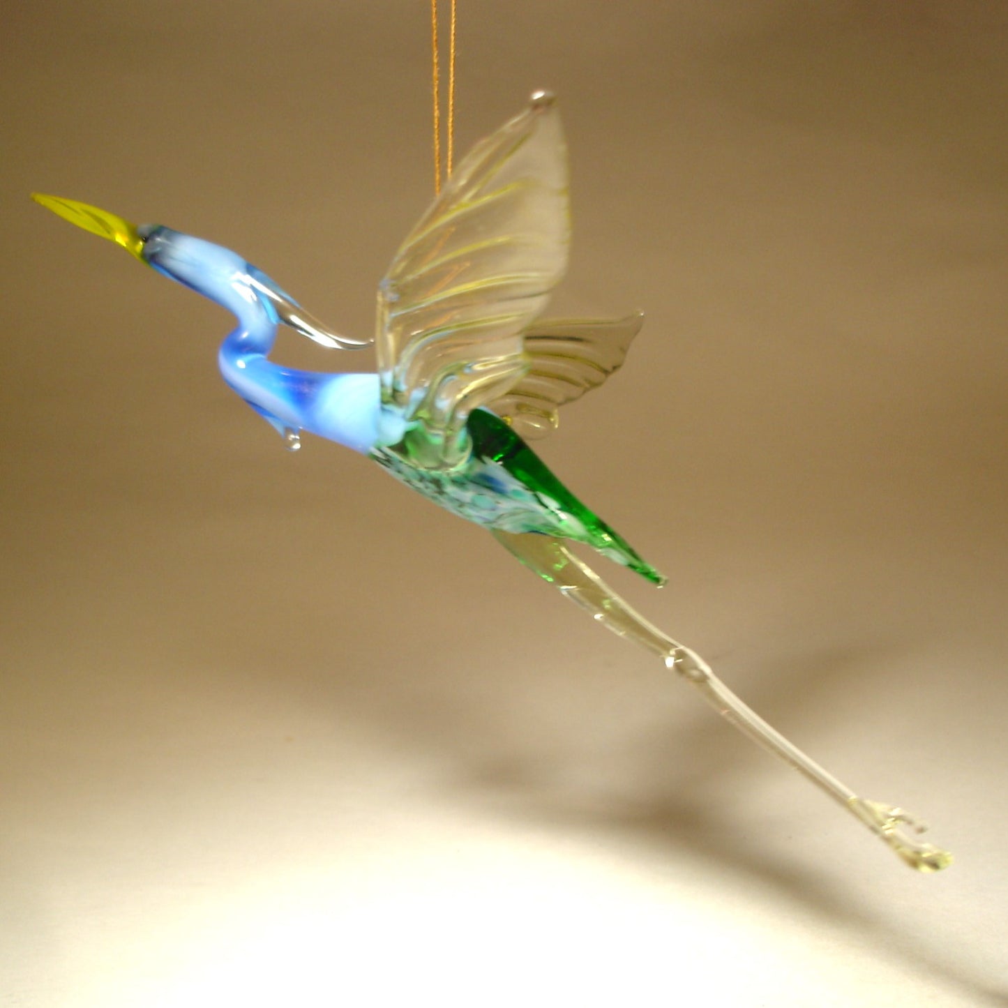 Side view of the Glass Heron in Flight Hanging Figurine, highlighting the bird's graceful posture and elongated neck mid-flight.