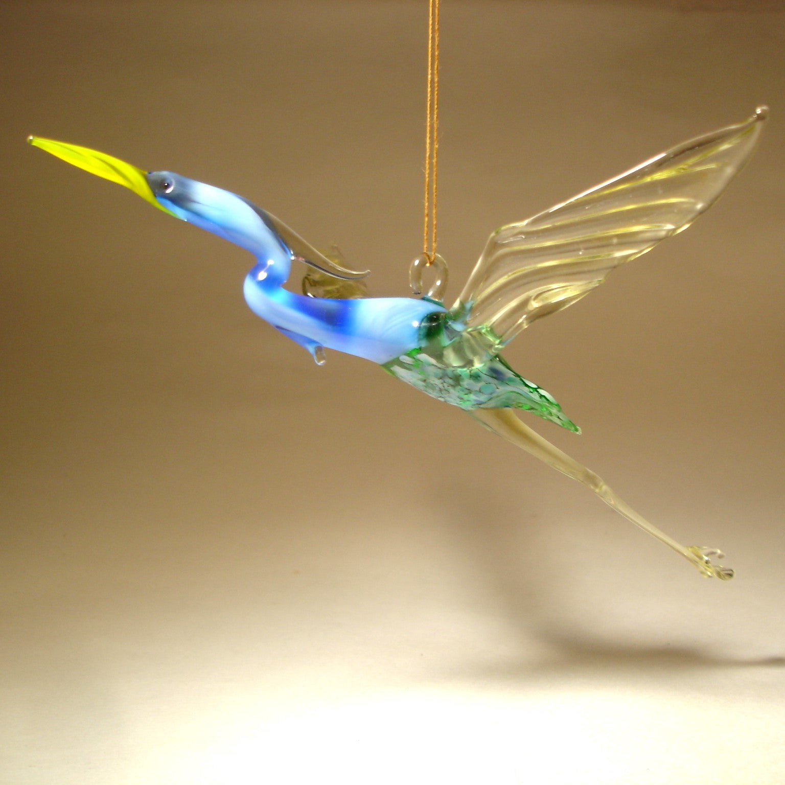 Angled view of the Glass Heron in Flight Hanging Figurine Ornament, showcasing its blue and green body and long legs.