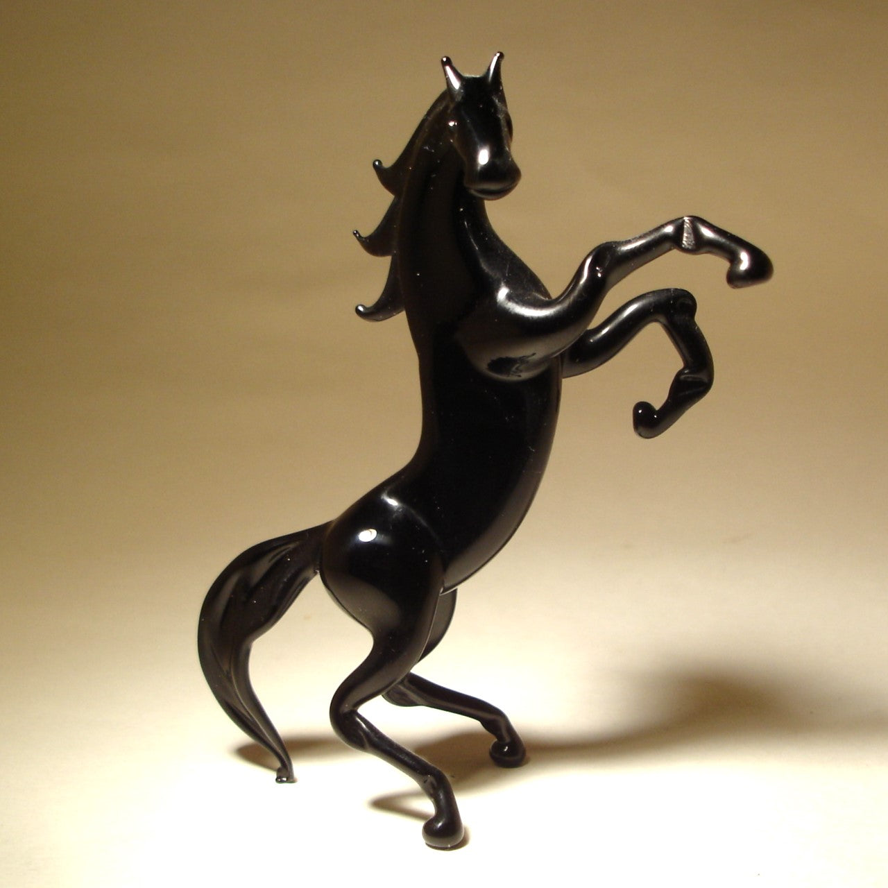 A side view of the rearing black glass horse figurine, emphasizing the graceful arch of its neck and the powerful position of its legs.