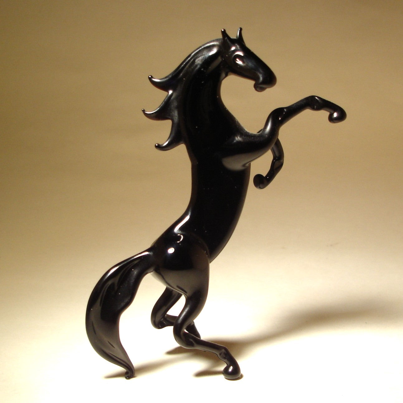 A front view of a rearing black glass horse figurine, showcasing its muscular build and detailed features, with its front legs lifted high.