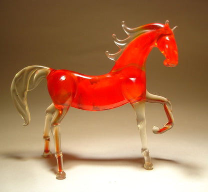 A side view of a red glass horse figurine, highlighting its raised left foot and flowing tail.