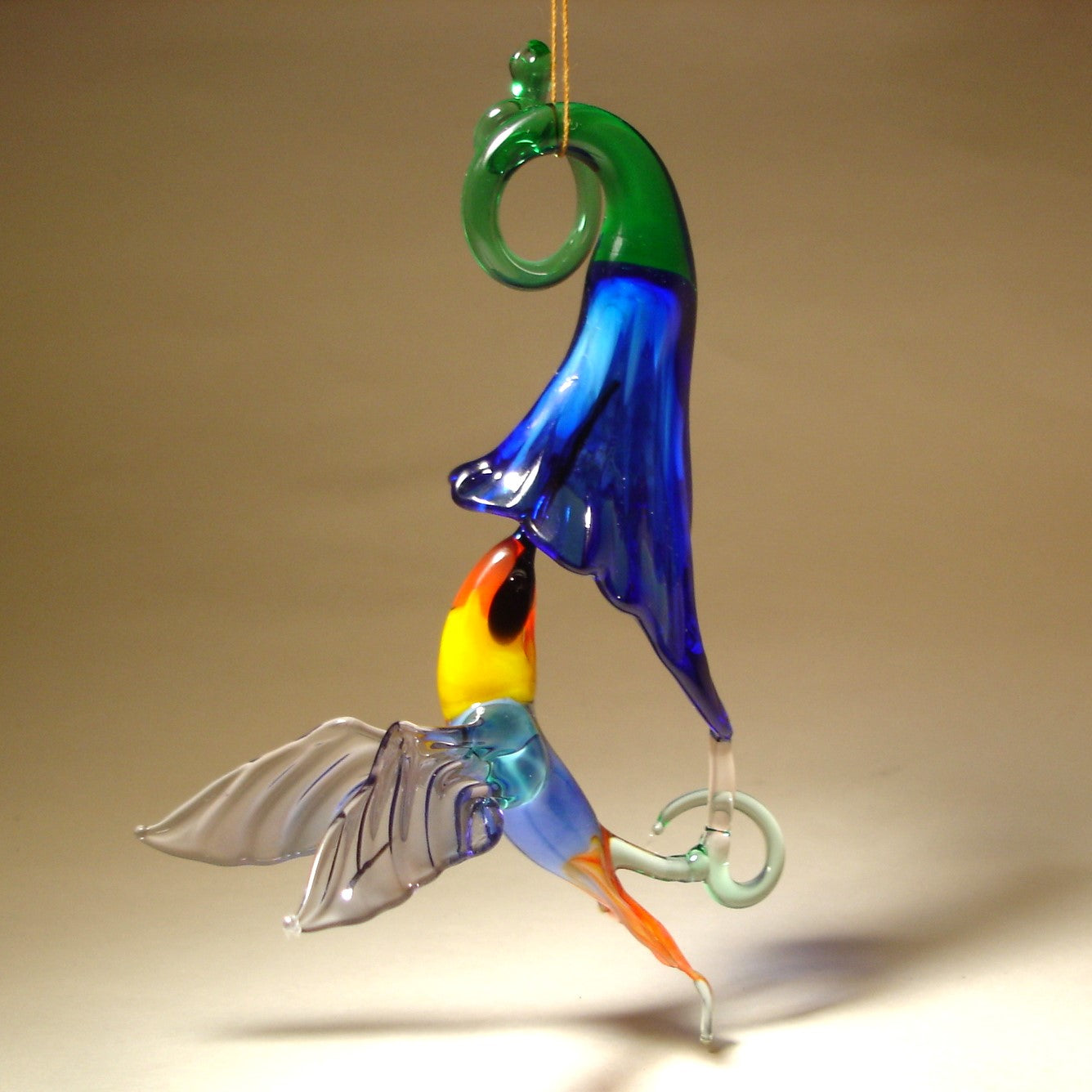 Glass ornament featuring a hummingbird drinking nectar from a blue trumpet flower.