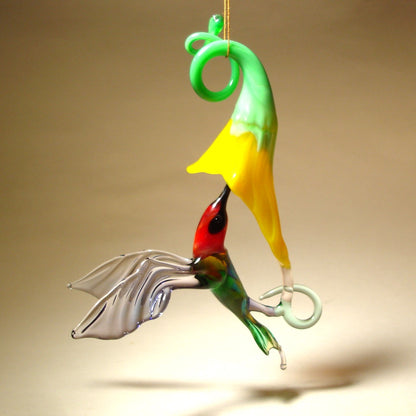 Another view of the red, green glass hummingbird with lilac wings shipping nectar from the yellow flower.