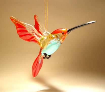 A side view of the red and blue glass hummingbird ornament, emphasizing the elegant curve of its body and wings.