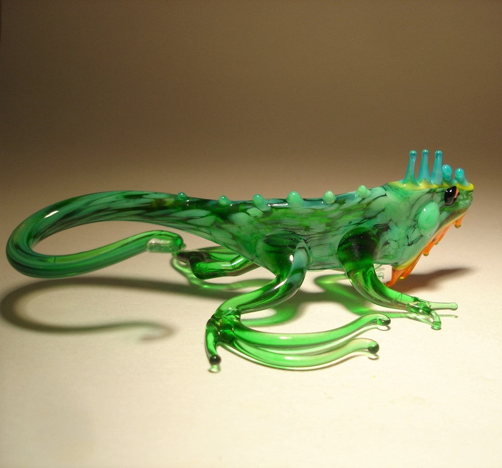 A glass iguana figurine in a striking pose, with its tail elegantly curved and intricate blue details on its head and orange beard.