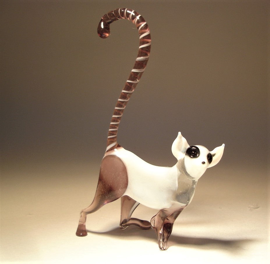 Side view of a white and lilac glass monkey lemur figurine, illustrating its dynamic pose with a curled striped tail. 