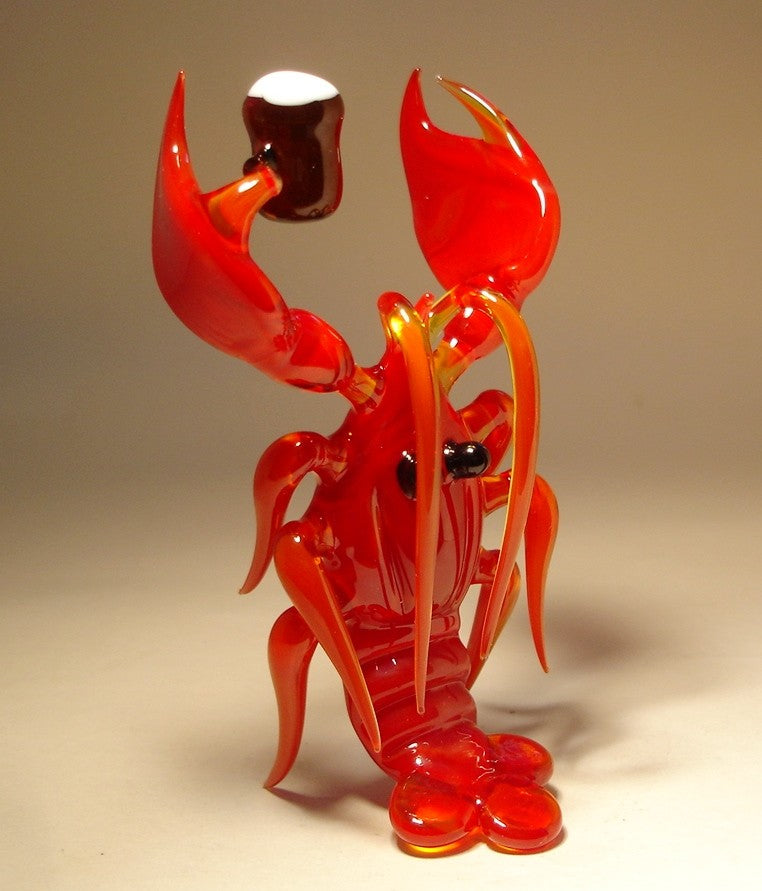 A side view of a red glass lobster figurine grasping a small beer keg, showcasing intricate details in the claws, legs, and curved tail.