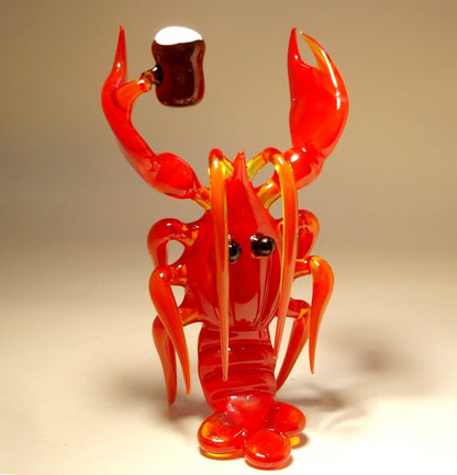 A front view of a red glass lobster figurine holding a miniature beer keg, with detailed claws and drooped antennae.