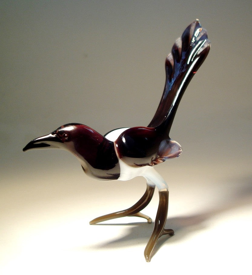 Side view of a glass magpie figurine, highlighting its distinctive long tail and black and white body.