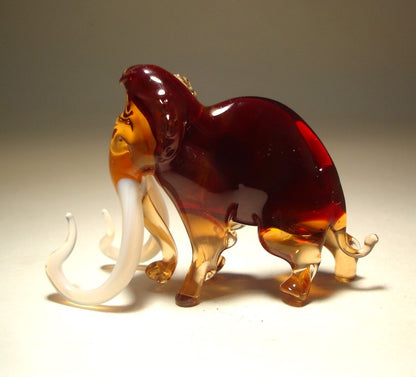 A side profile of the glass mammoth figurine, highlighting its impressive tusks and the elegant curvature of its body.