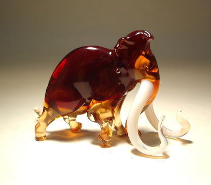 A detailed glass mammoth figurine with long, curved tusks, depicted in a walking position.