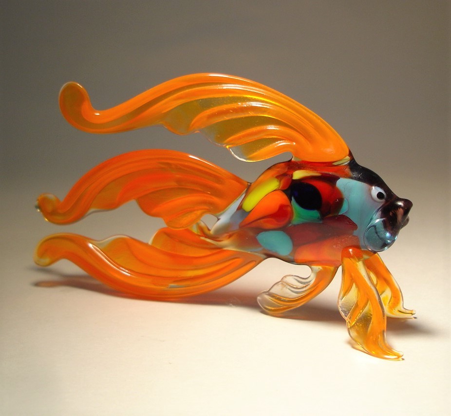 A side view of the orange Betta fish glass figurine, highlighting the flowing, fan-like fins and tail that extend gracefully behind the fish.