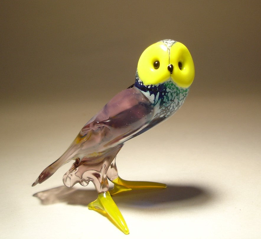 Close-up of a lilac and green glass owl figurine featuring a bright yellow face and feet.