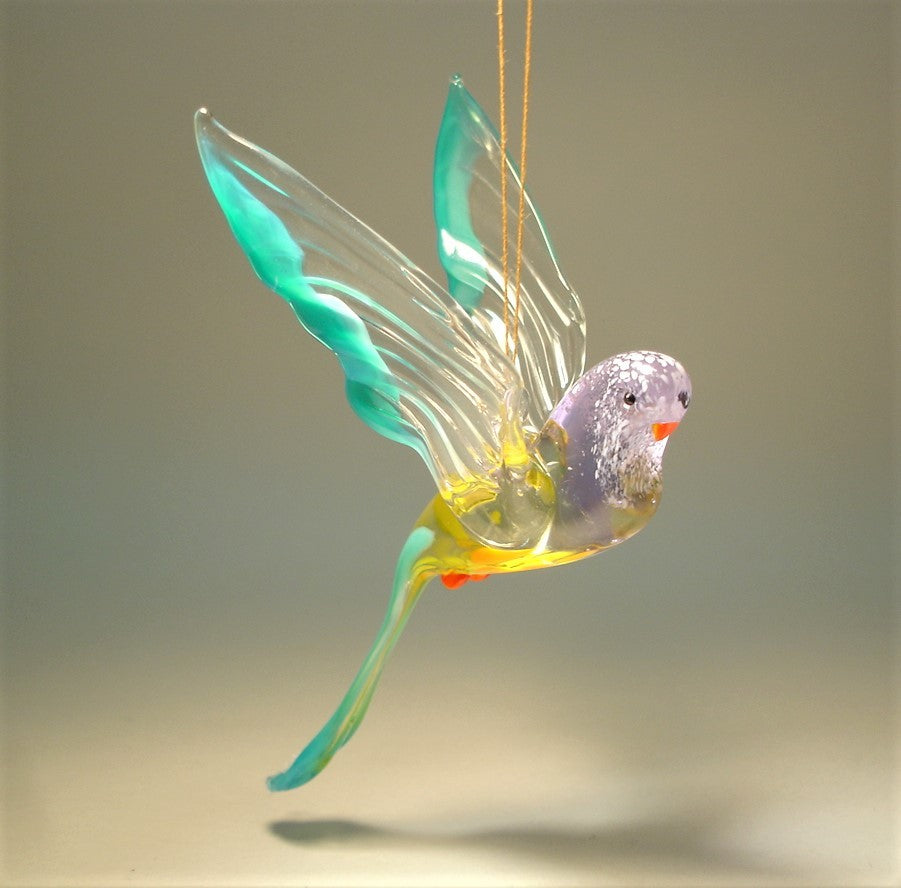 The glass parakeet ornament is depicted in striking blue and yellow hues and red beak.