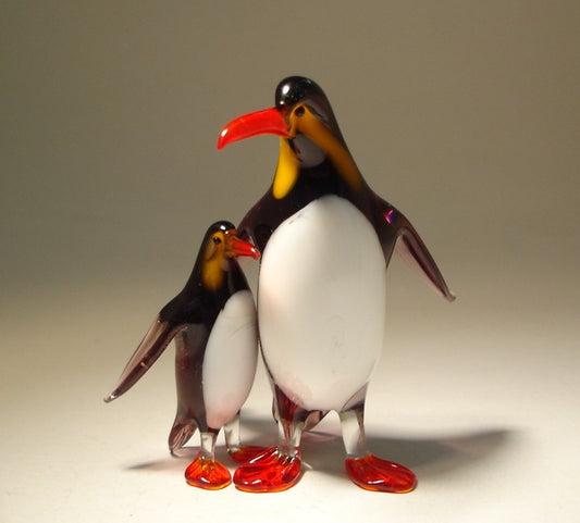 Close-up of a glass penguin figurine with a baby penguin nestled close to its body, creating a warm, loving scene.