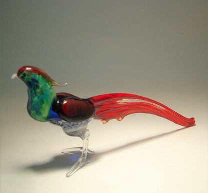 A close-up view of a vibrant glass pheasant figurine, showcasing its green and blue body and red tail.